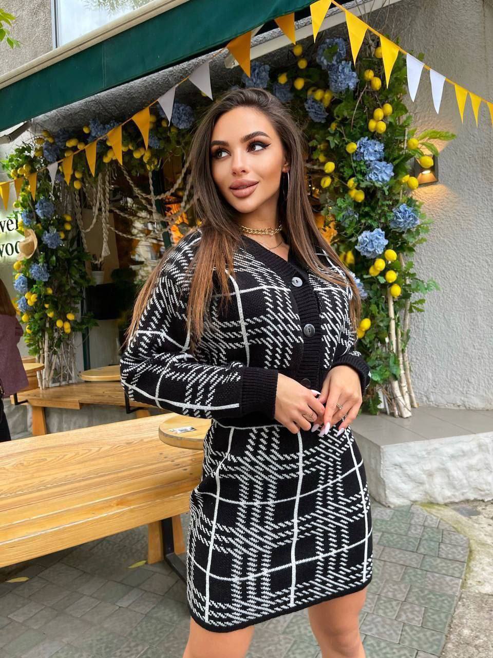 Woman wearing a black and white checkered dress standing in front of floral decorations.