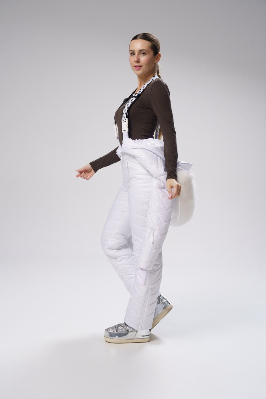 Woman wearing a brown top and white pants on a gray background