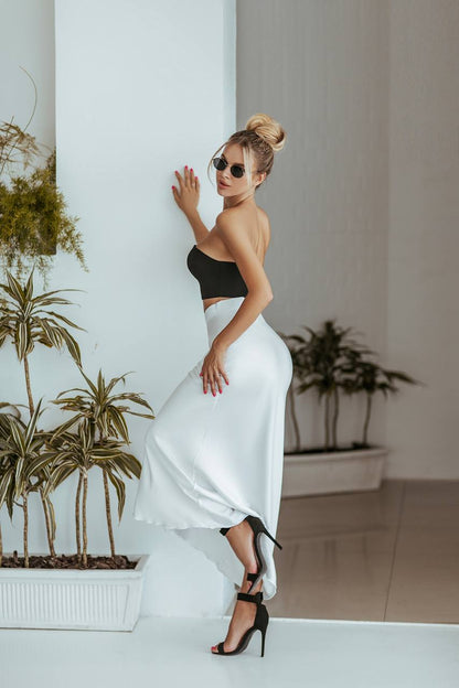 Woman in a black top and white skirt standing indoors with plants in the background