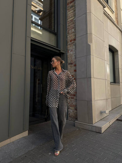 Woman standing outside a building entrance wearing a patterned shirt and jeans.