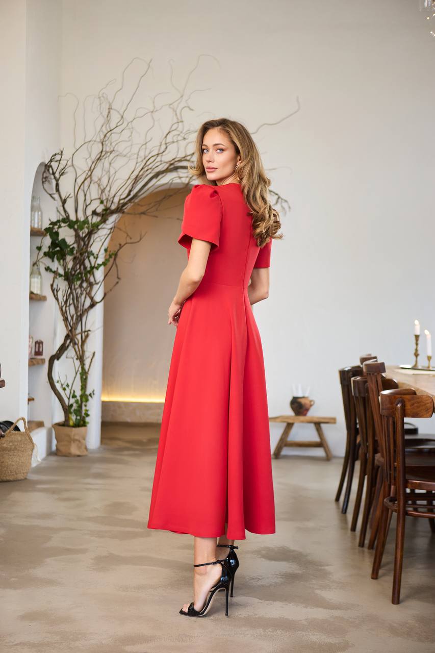 Woman in a red dress standing in a room with wooden flooring and furniture.
