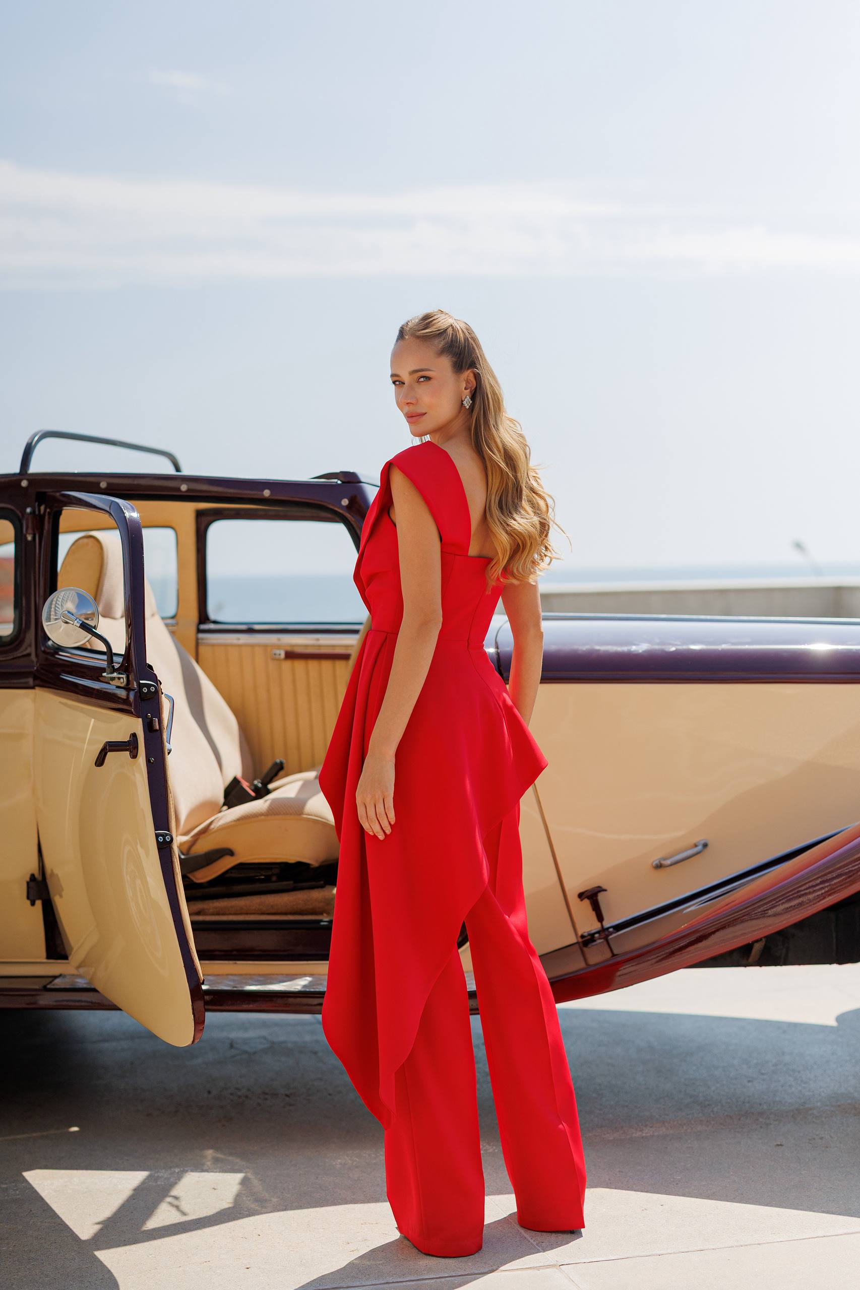 Woman in a red outfit standing next to an open car door with a scenic background