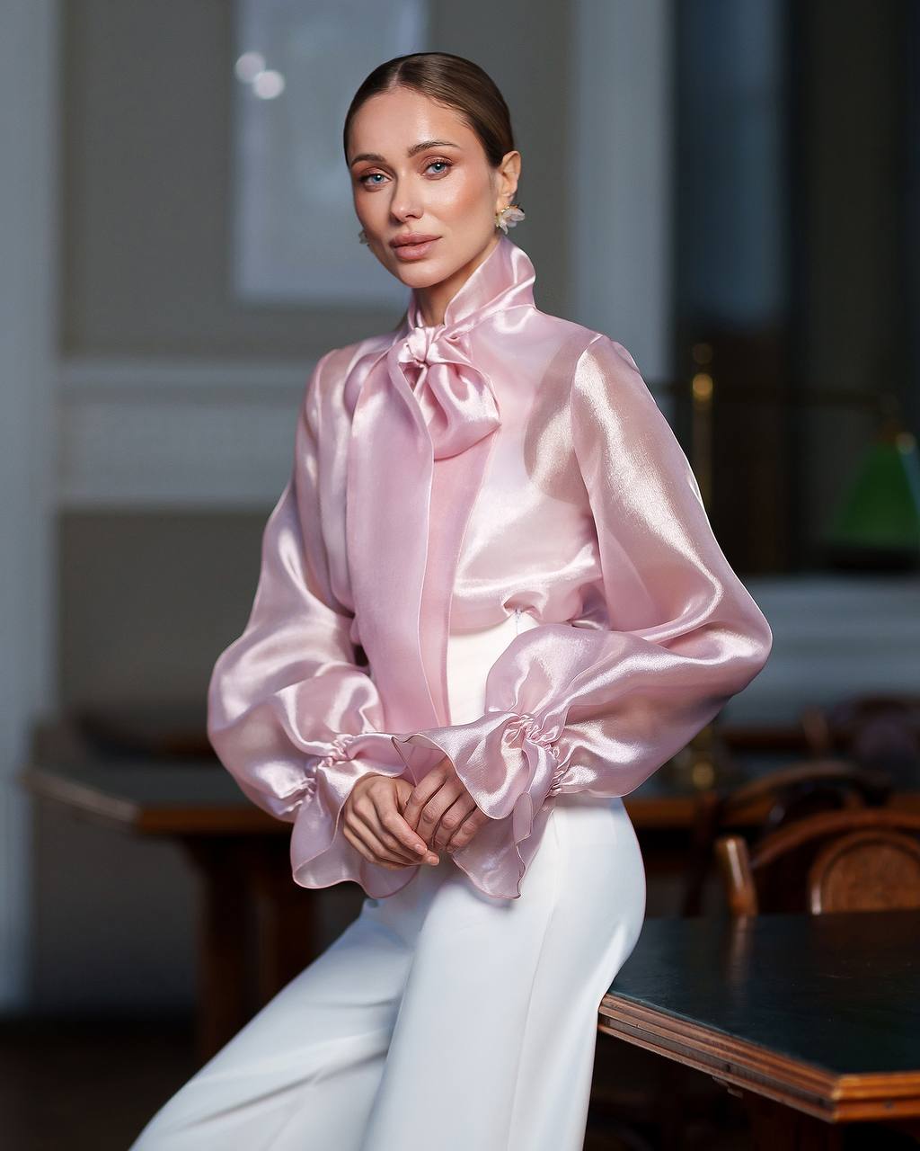 Woman wearing a pink satin blouse with a bow tie in an indoor setting