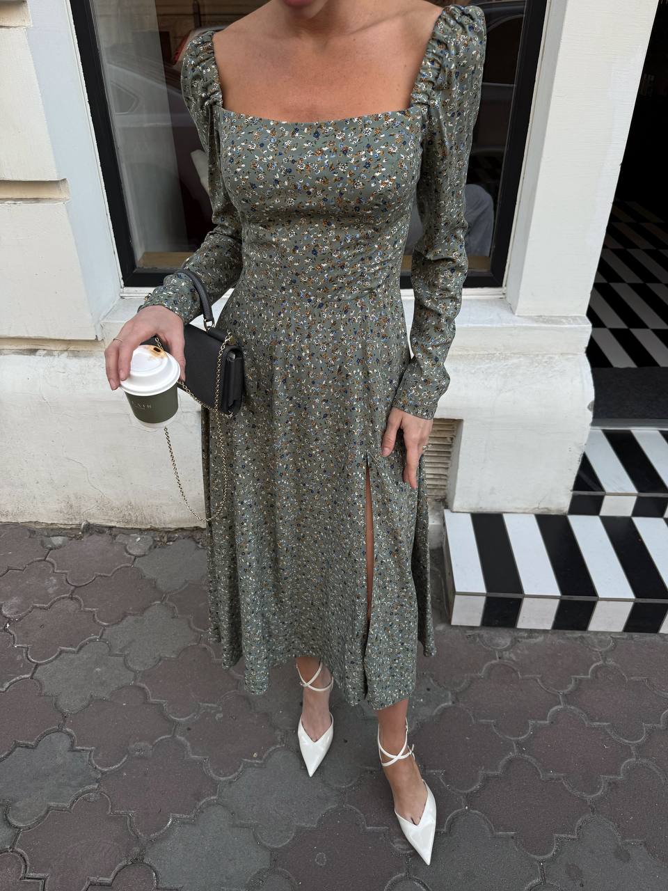 Woman in a green floral dress standing on a sidewalk.
