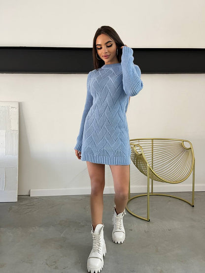 Woman wearing a blue knitted dress with white shoes in a minimalistic room.