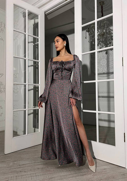 Woman in a long, dark patterned dress standing in a room with large windows.
