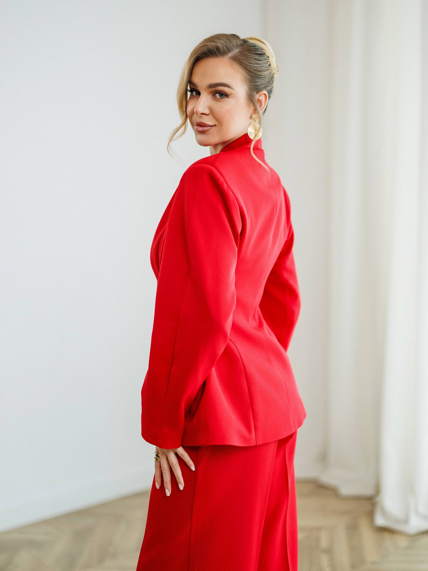 Woman wearing a red outfit standing against a white wall.