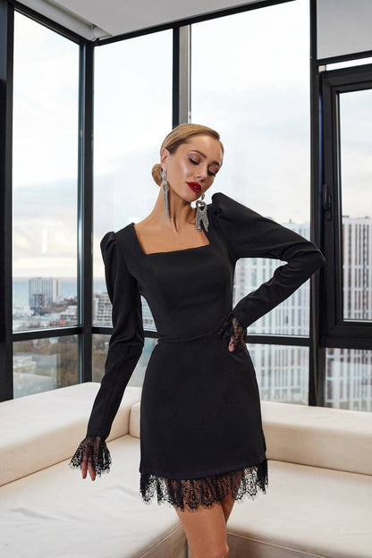 Woman in a black dress with lace details standing in front of large windows with a cityscape view.