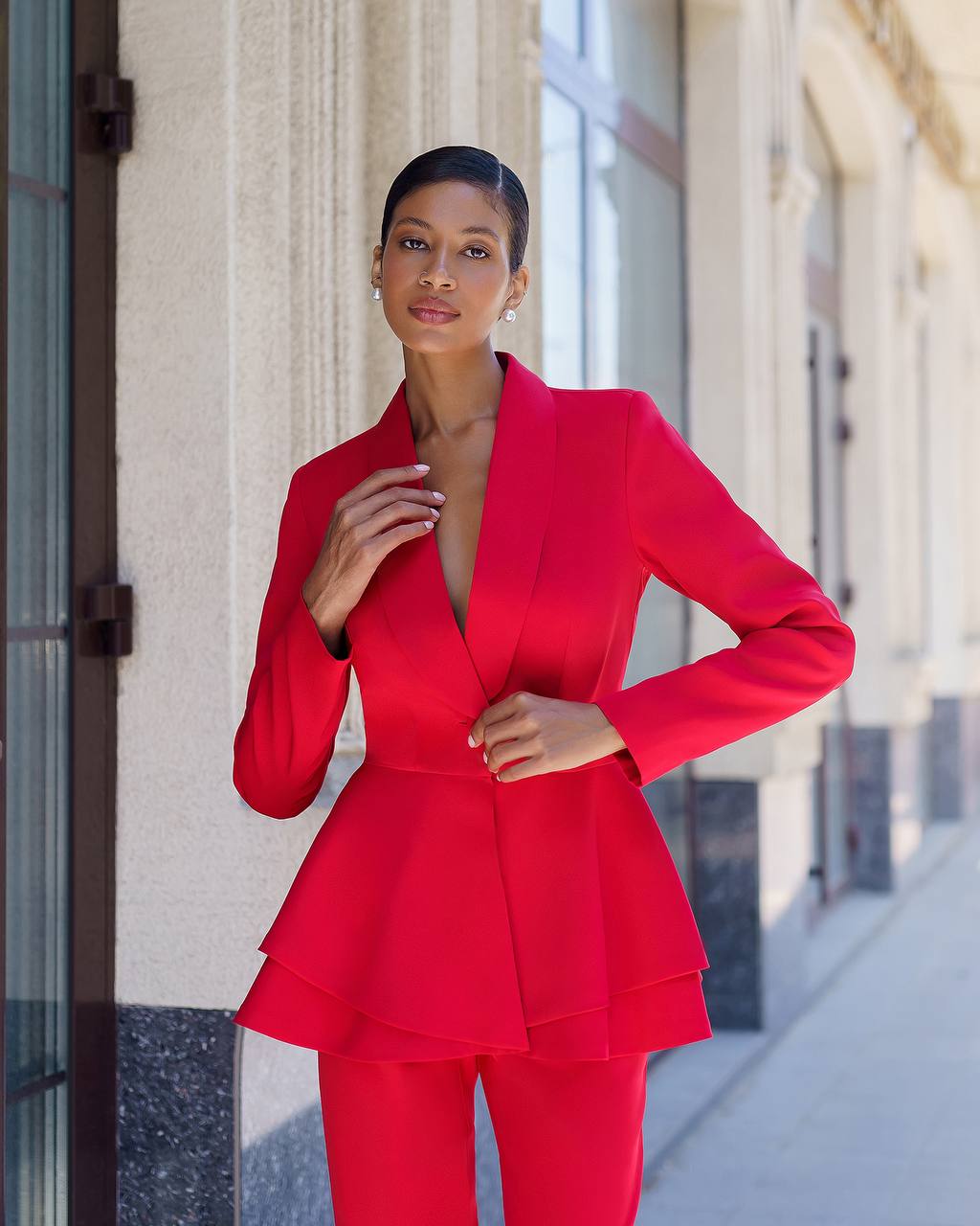 Woman in a red suit standing on a city street.