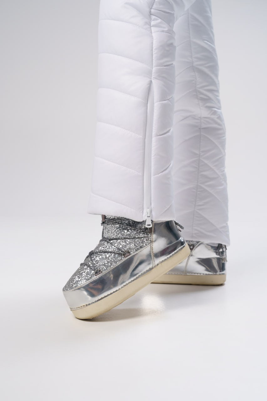 Silver glittery high-top sneakers worn with white pants on a light gray background