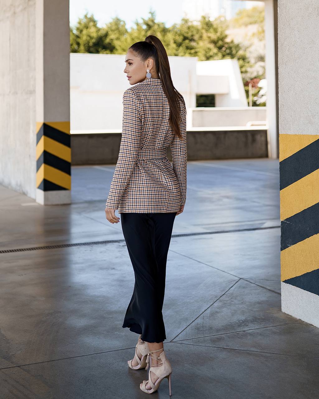 Woman in a plaid blazer and black pants walking in an urban setting.