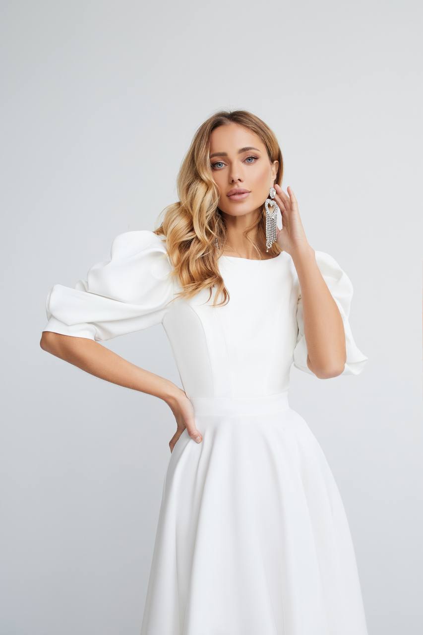 Woman wearing a white dress with puffed sleeves against a plain background