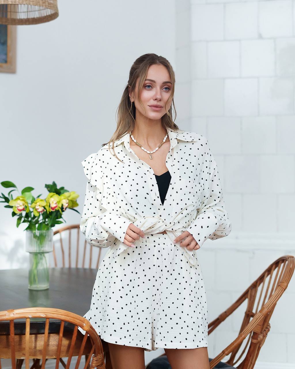 Woman wearing a white polka dot dress in a room with a table and chairs.