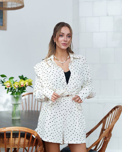Woman wearing a white polka dot dress in a room with a table and chairs.