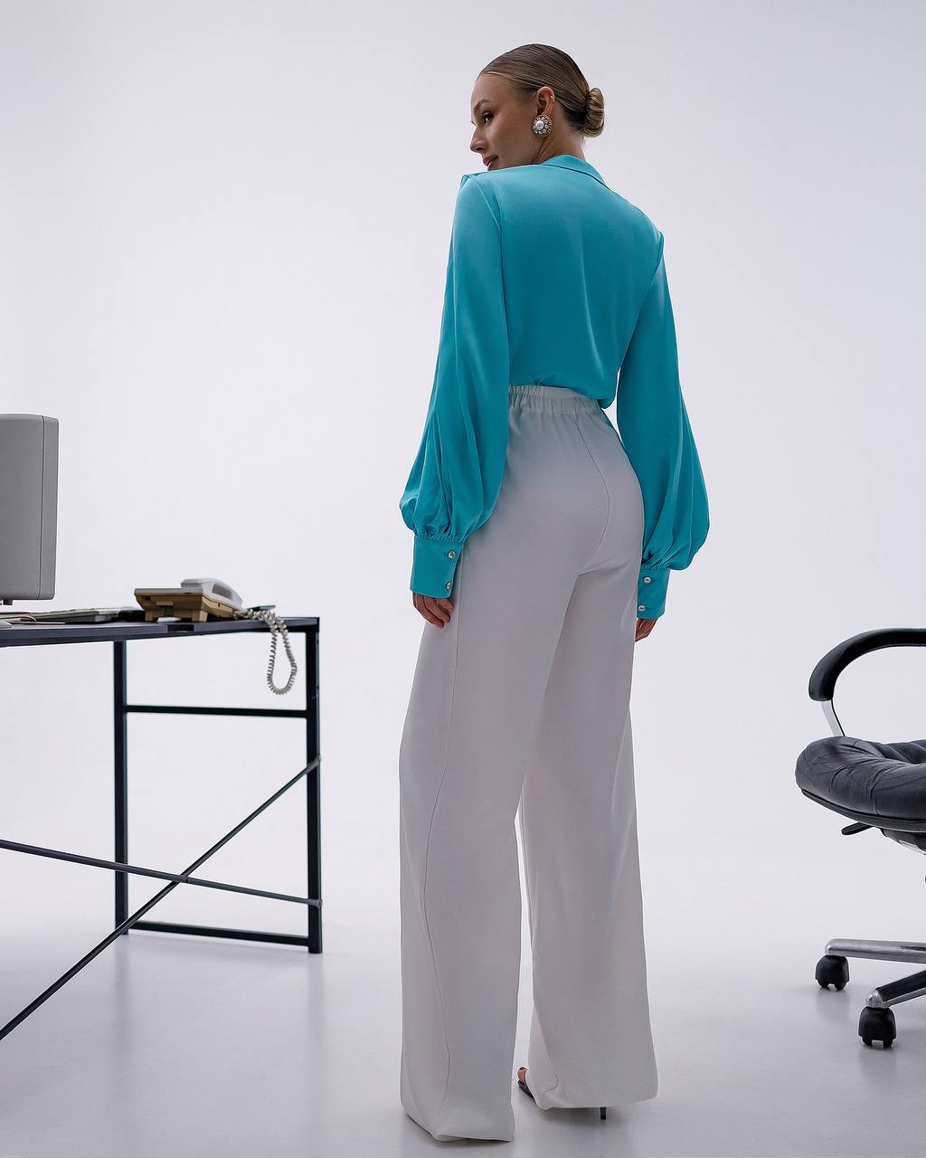 Person wearing a teal blouse and white pants in an office setting