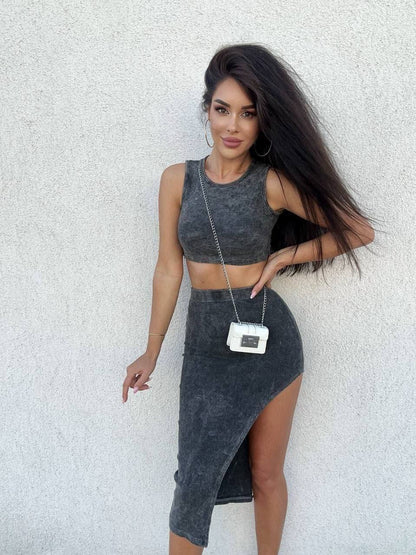 Woman in gray sleeveless top and skirt with a white handbag against a light gray wall.