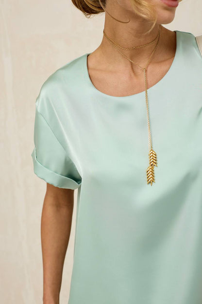 Person wearing a light green top and a gold necklace with an arrow pendant on a beige background