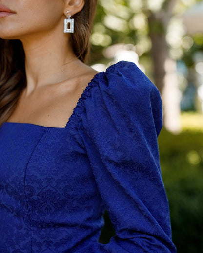 Close-up of a person wearing a blue lace dress with a blurred outdoor background