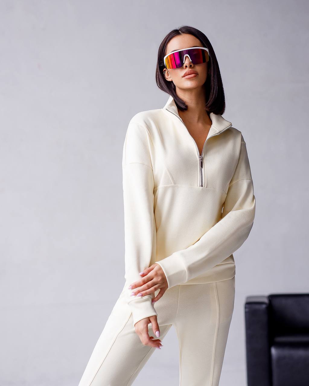 Person wearing a white outfit with colorful sunglasses on a gray background