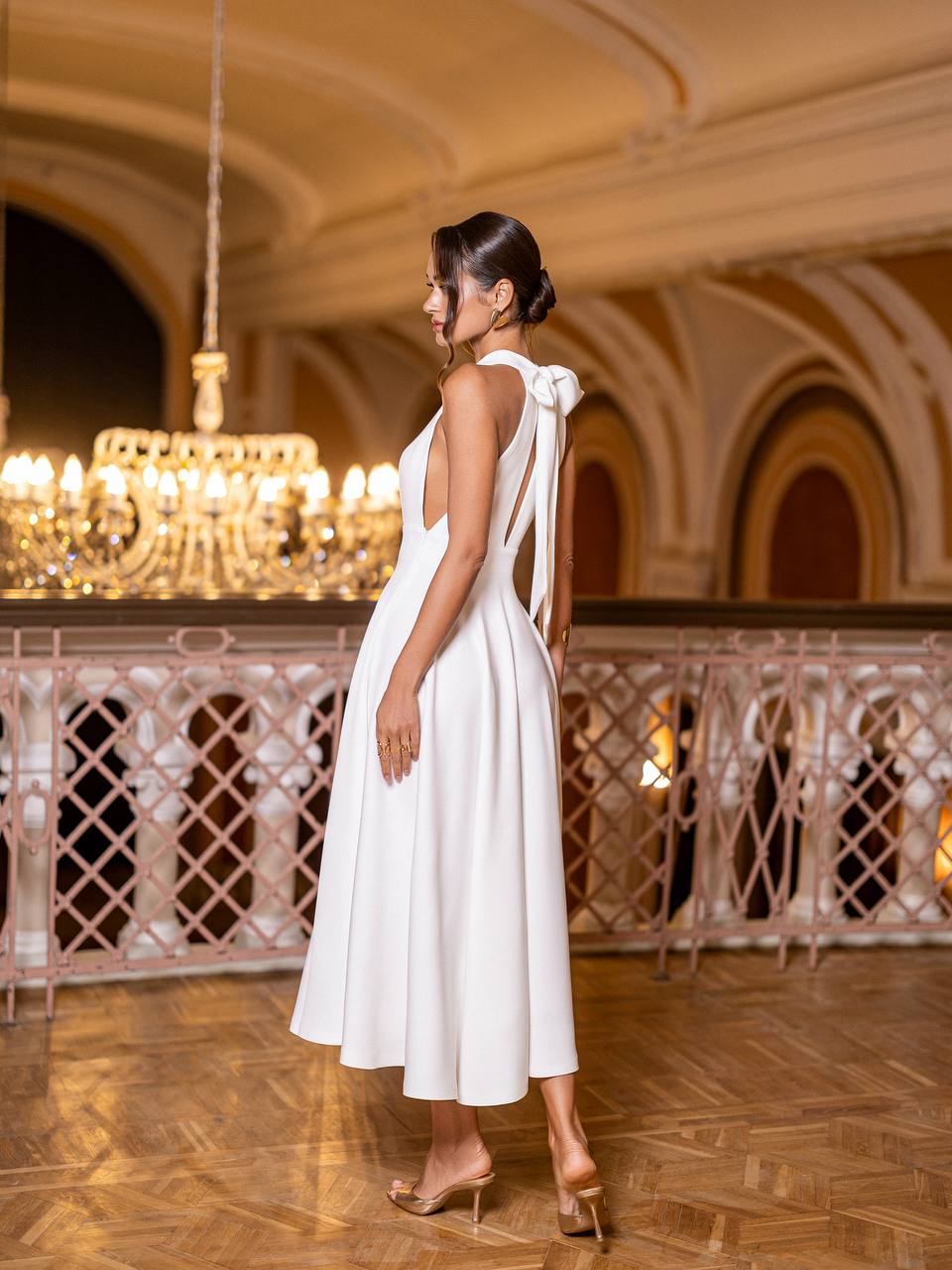 Woman in a white dress standing in an elegant interior setting with chandeliers.