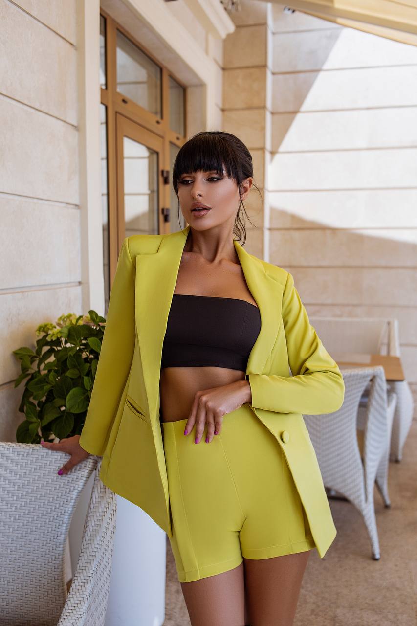 Woman in a bright yellow suit standing outdoors near a building entrance.