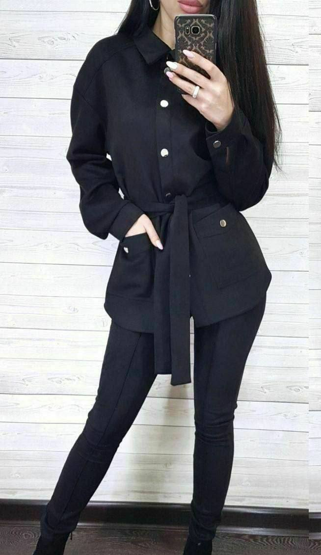 Person wearing a black outfit with a belt against a white wall