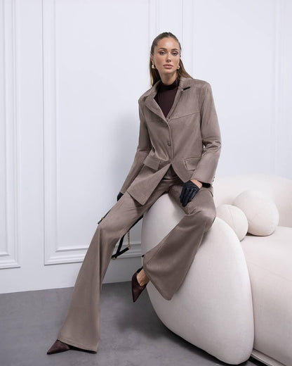 Woman in a beige suit sitting on a white chair against a white wall.