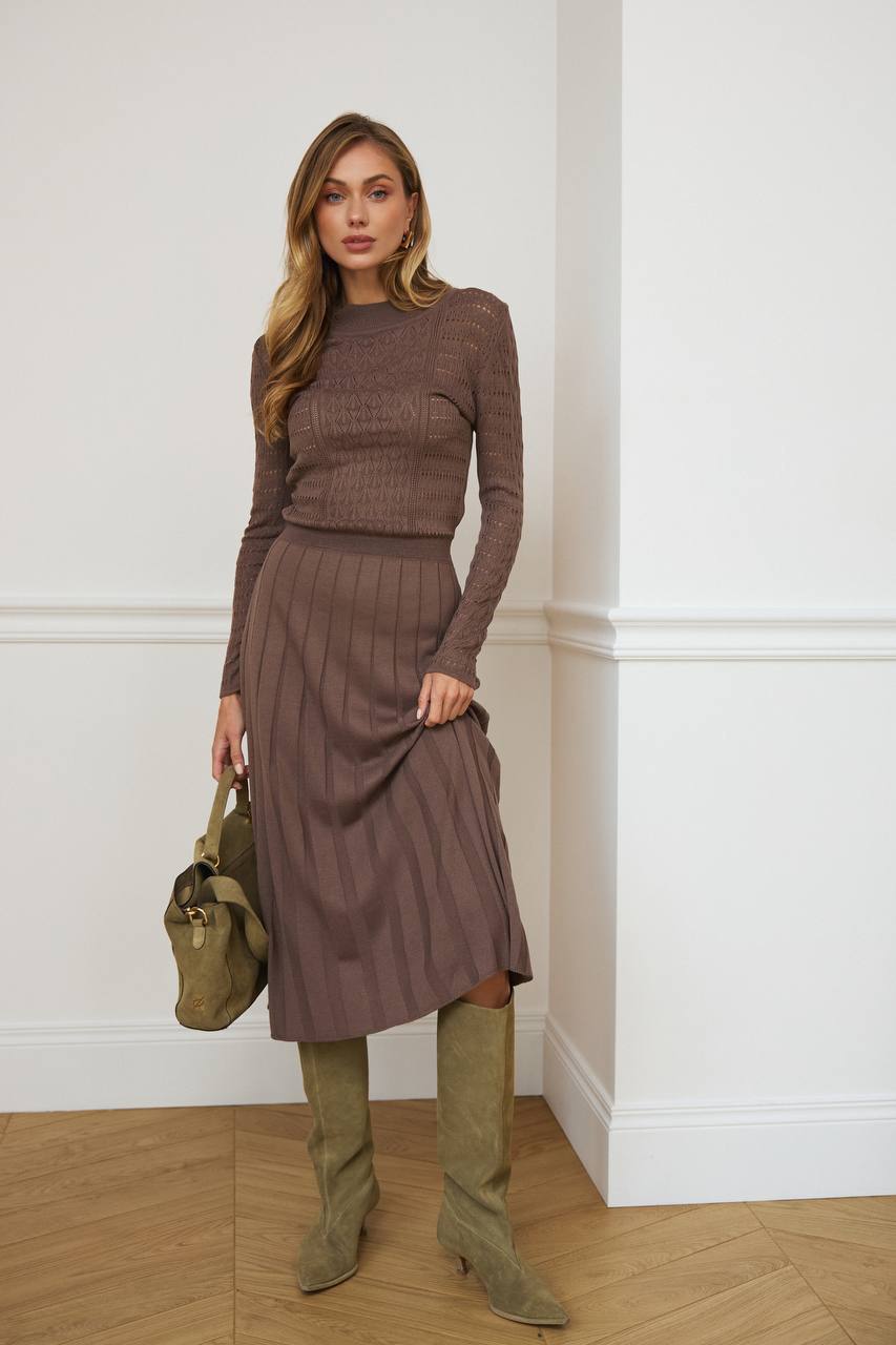 Woman wearing a brown ribbed knit dress with matching top and green boots, holding a green bag indoors.