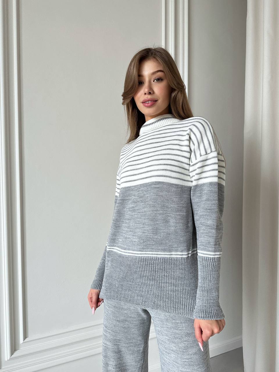 Woman wearing a gray and white striped sweater and pants against a neutral background