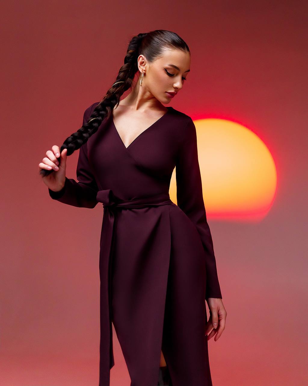 Woman in a dark purple dress with a braided hairstyle against a sunset background