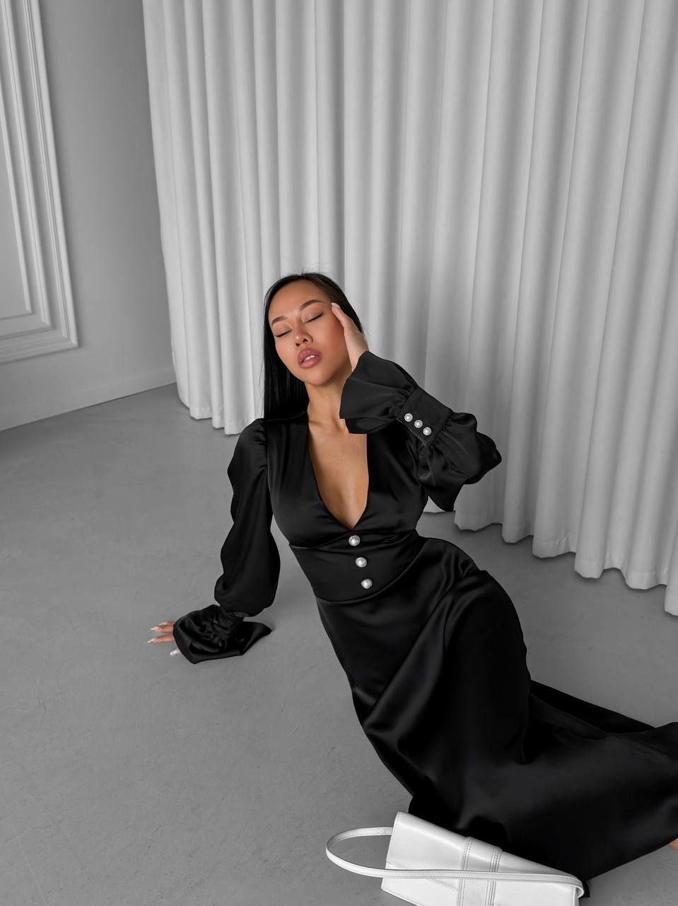 Woman in a black outfit sitting on the floor against a gray curtain background