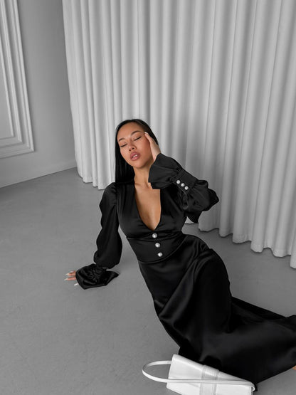 Woman in a black outfit sitting on the floor against a gray curtain background