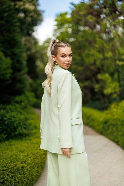 Woman in a light green outfit standing on a path with greenery around