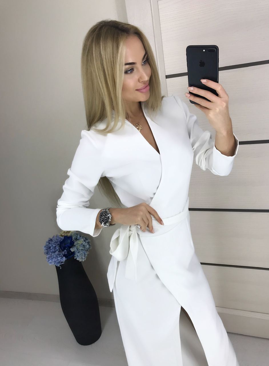 Woman in a white outfit taking a mirror selfie in a minimalistic room.