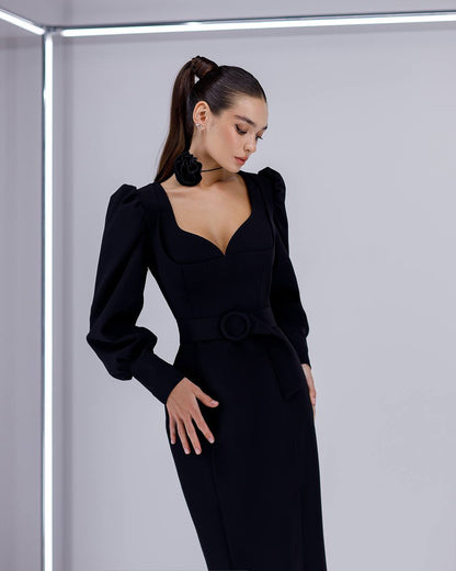 Woman wearing a black dress with puffed sleeves against a light gray background