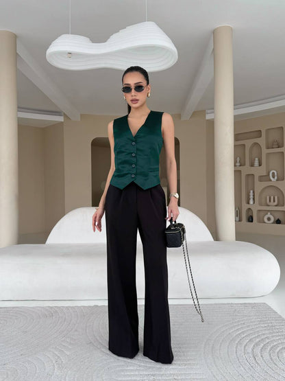 Woman in a green vest and black pants standing in a modern interior setting.