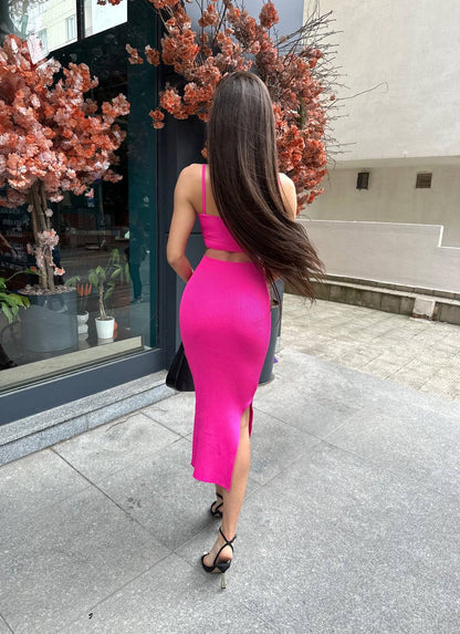 Woman in a bright pink dress walking outdoors near a building entrance.