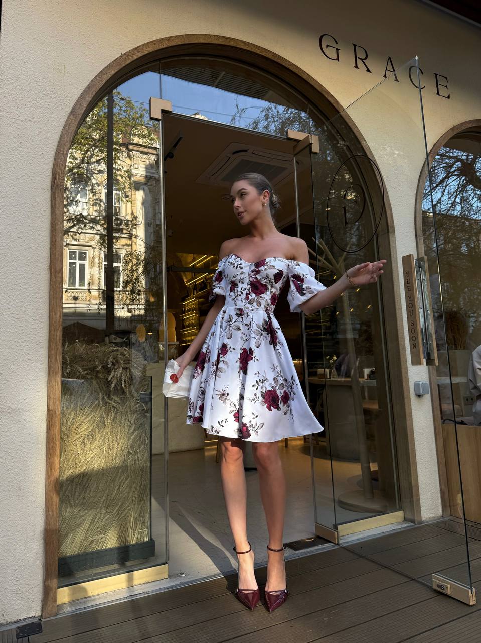 Woman in a floral dress standing outside a store named 'Grace'.