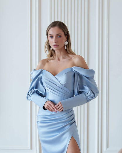 Woman wearing a light blue off-shoulder dress against a white wall.
