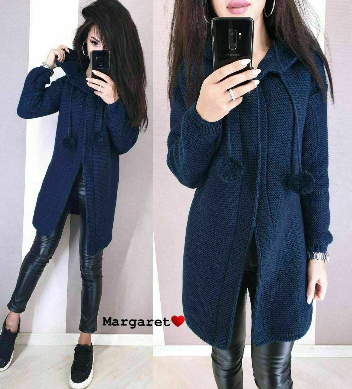 Woman wearing a navy blue coat with pom-pom details, taking a mirror selfie.