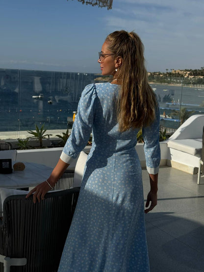 Woman in a blue dress standing on a balcony with a scenic view of water and buildings.