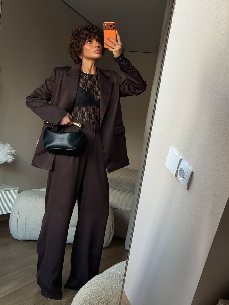 Person taking a mirror selfie wearing a brown outfit with a black bag in a room.