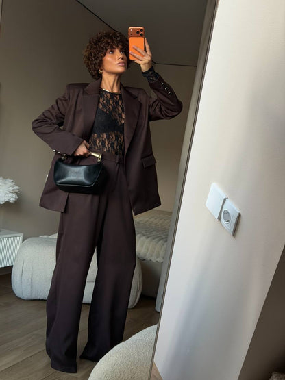 Person taking a mirror selfie wearing a brown outfit with a black bag in a room.