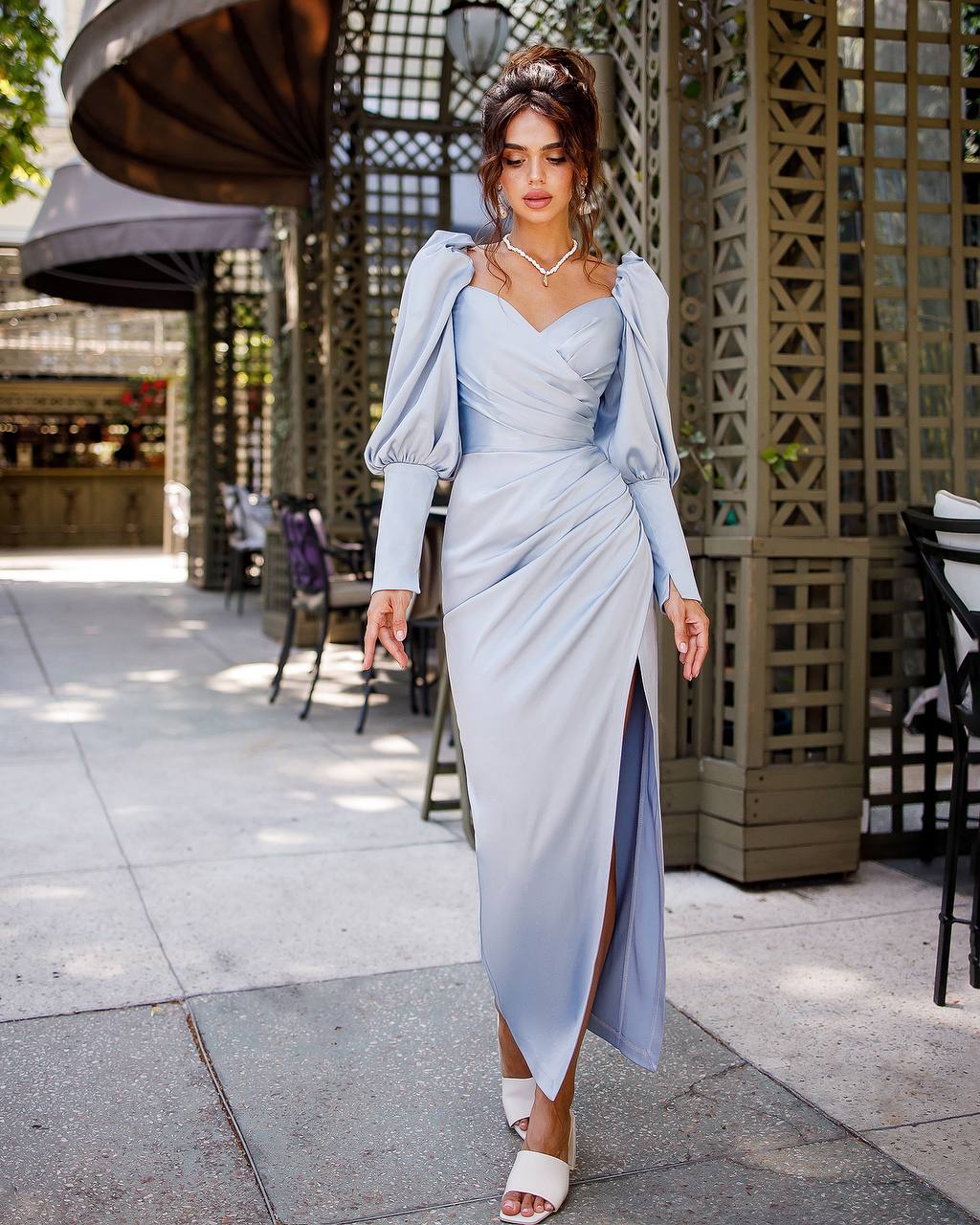 Woman in a light blue dress and matching jacket walking outdoors.