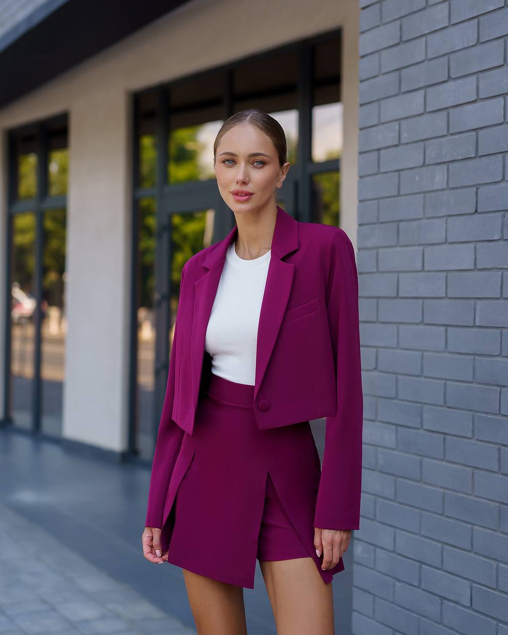 Woman in a magenta suit standing against a brick wall.