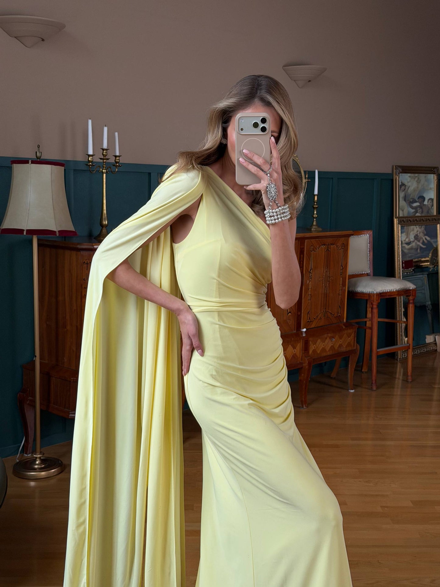 Woman in a yellow dress taking a mirror selfie in an indoor setting.