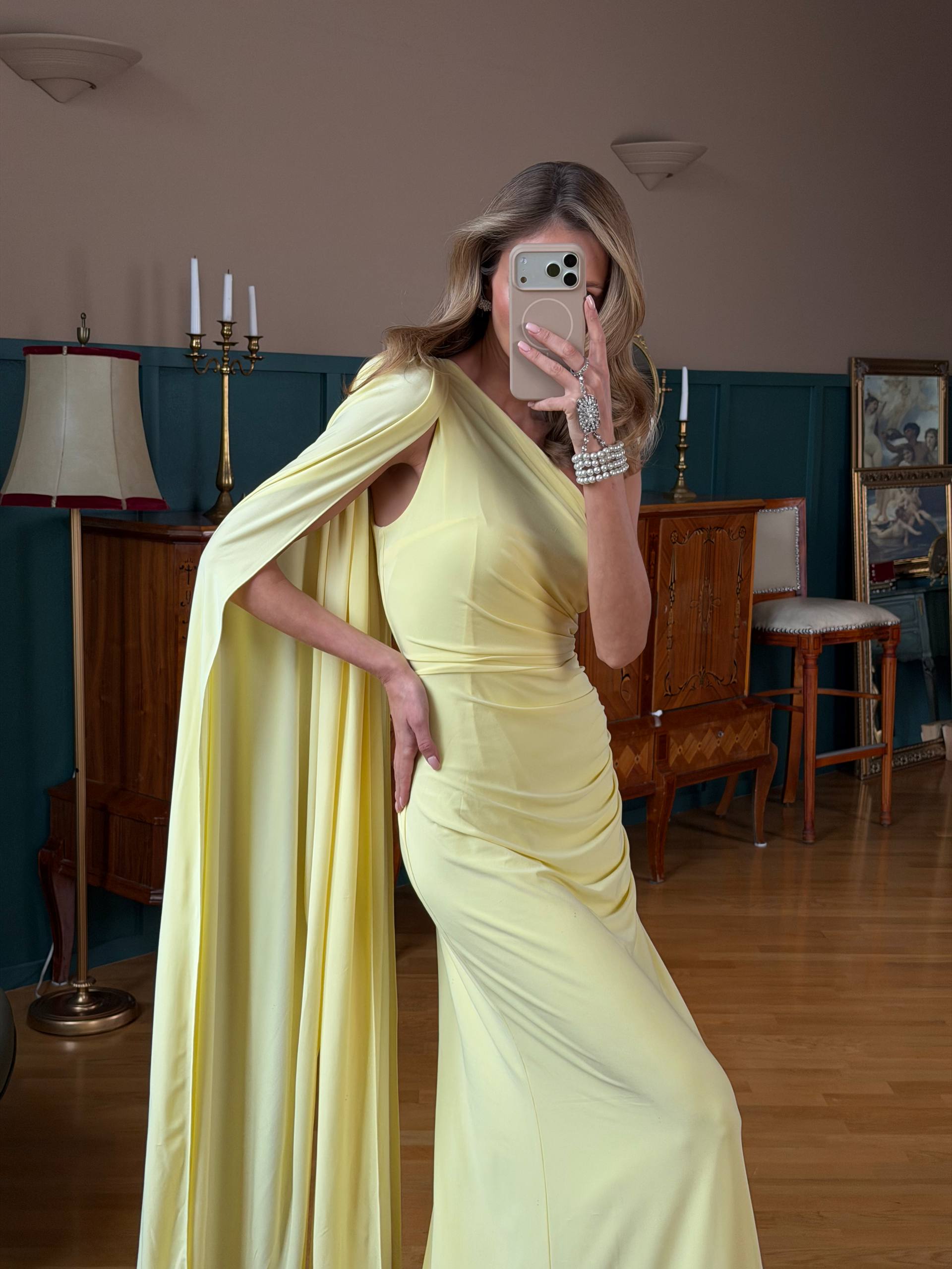 Woman in a yellow dress taking a mirror selfie in an indoor setting.