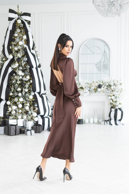 Woman in a brown dress standing in a decorated room with a Christmas tree and floral arrangements.