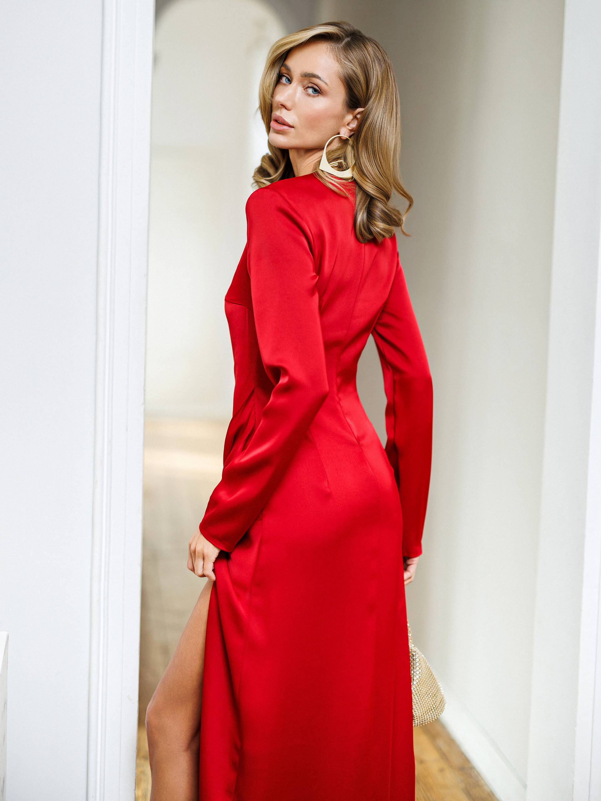 Woman wearing a red dress with a high slit, standing in a well-lit room.