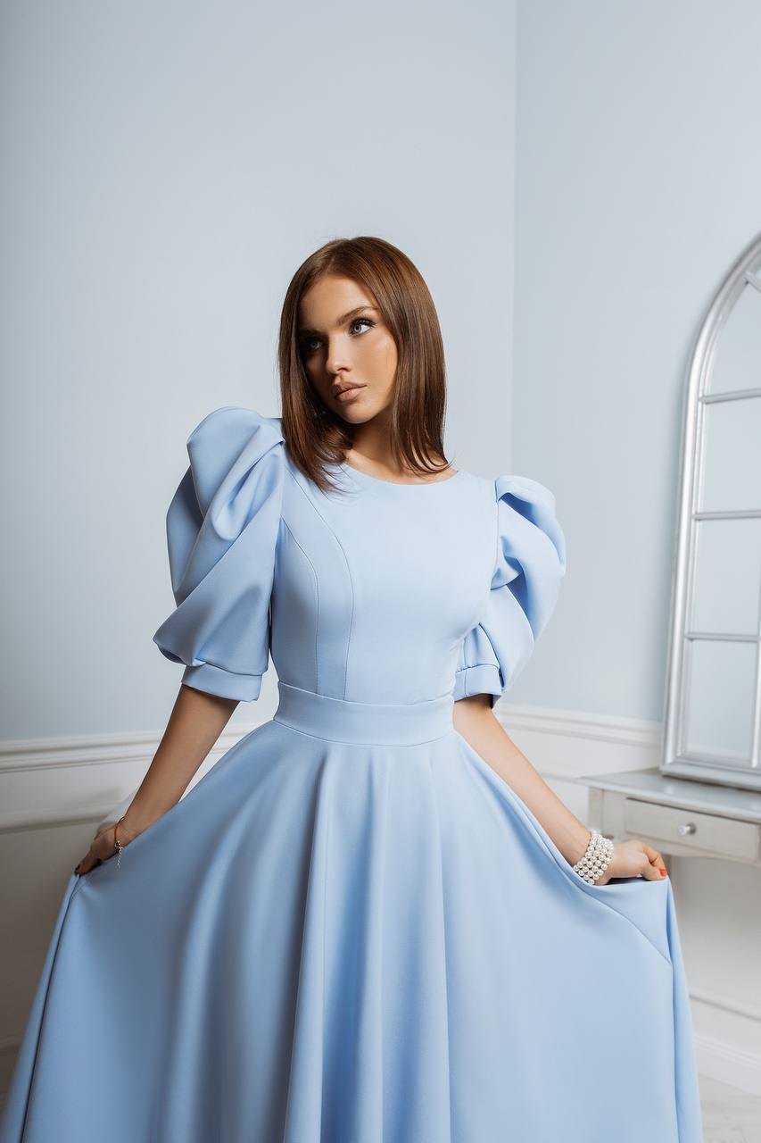 Woman wearing a light blue dress with puffed sleeves in an elegant room.
